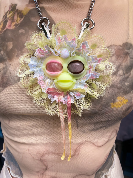 yellow face pendant with rose quartz eyes, white and yellow lace ruff, and pastel rainbow bow, front view