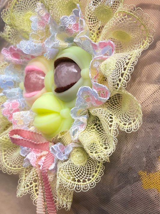 yellow face pendant with rose quartz eyes, white and yellow lace ruff, and pastel rainbow bow, 3/4 view